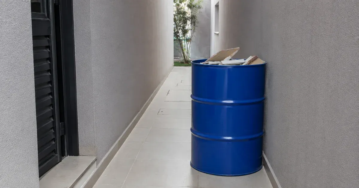 Tambor metálico azul de 200 litros posicionado em espaço reduzido de condomínio, ocupando pouco espaço